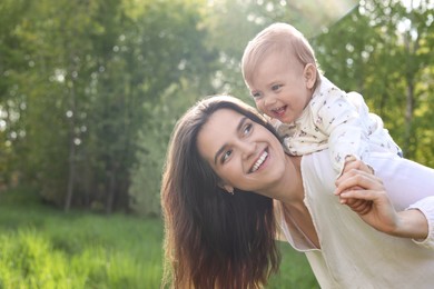 Photo of Happy mother playing with her cute baby in park on sunny day, space for text