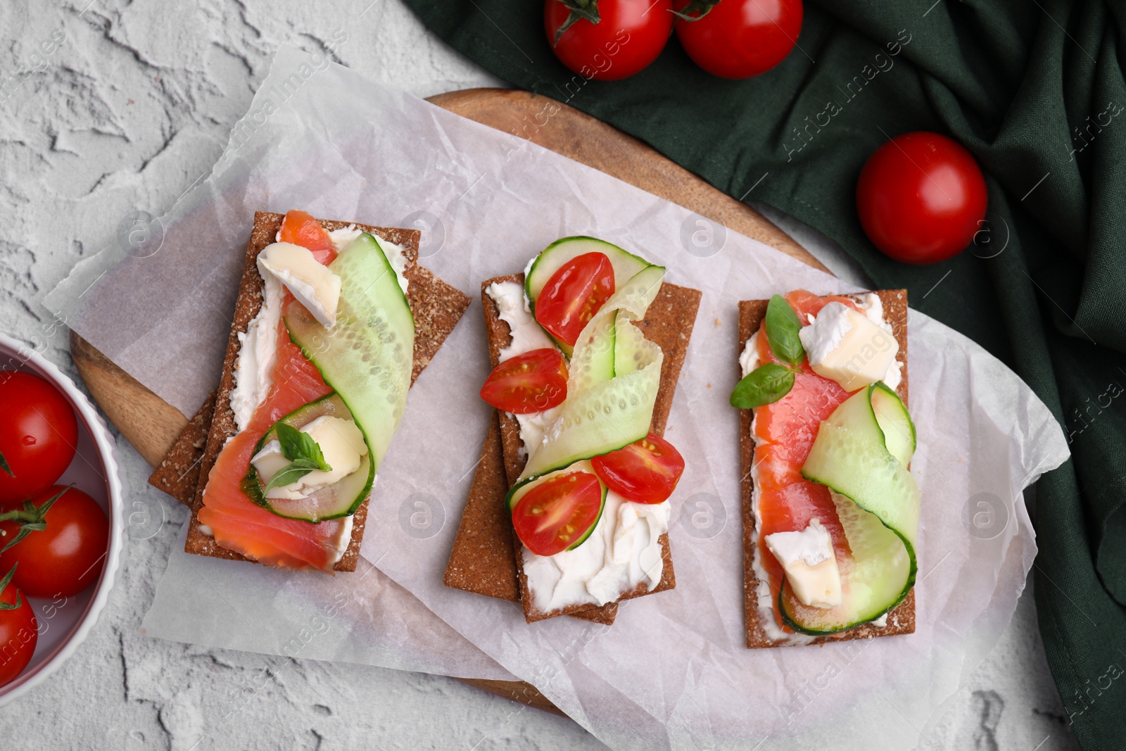 Photo of Tasty rye crispbreads with salmon, cream cheese and vegetables on grey textured table, flat lay