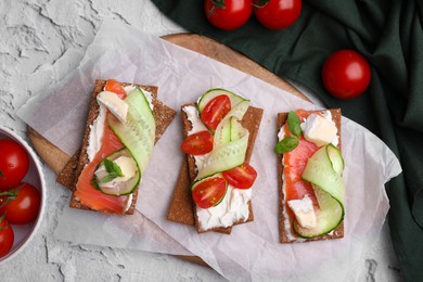 Photo of Tasty rye crispbreads with salmon, cream cheese and vegetables on grey textured table, flat lay
