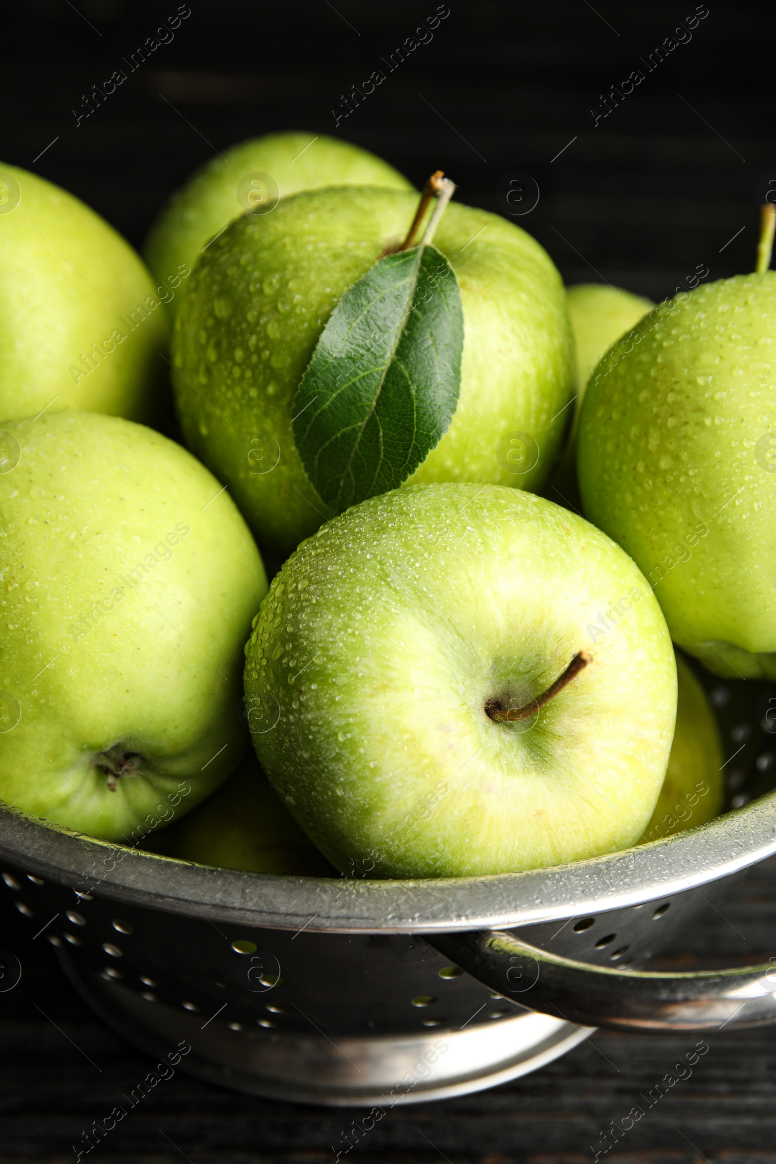 Photo of Colander of fresh ripe green apples on black wooden table, closeup view