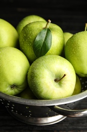 Colander of fresh ripe green apples on black wooden table, closeup view