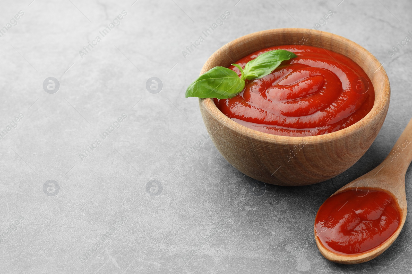Photo of Bowl and spoon of tasty ketchup with basil on light grey table, closeup. Space for text
