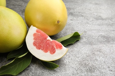 Photo of Fresh cut and whole pomelo fruits with leaves on grey table, closeup. Space for text