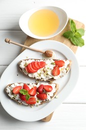 Photo of Delicious ricotta bruschettas with strawberry, mint and pistachios served with honey on white wooden table, flat lay