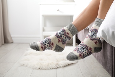 Woman wearing knitted socks on bed indoors, closeup. Warm clothes