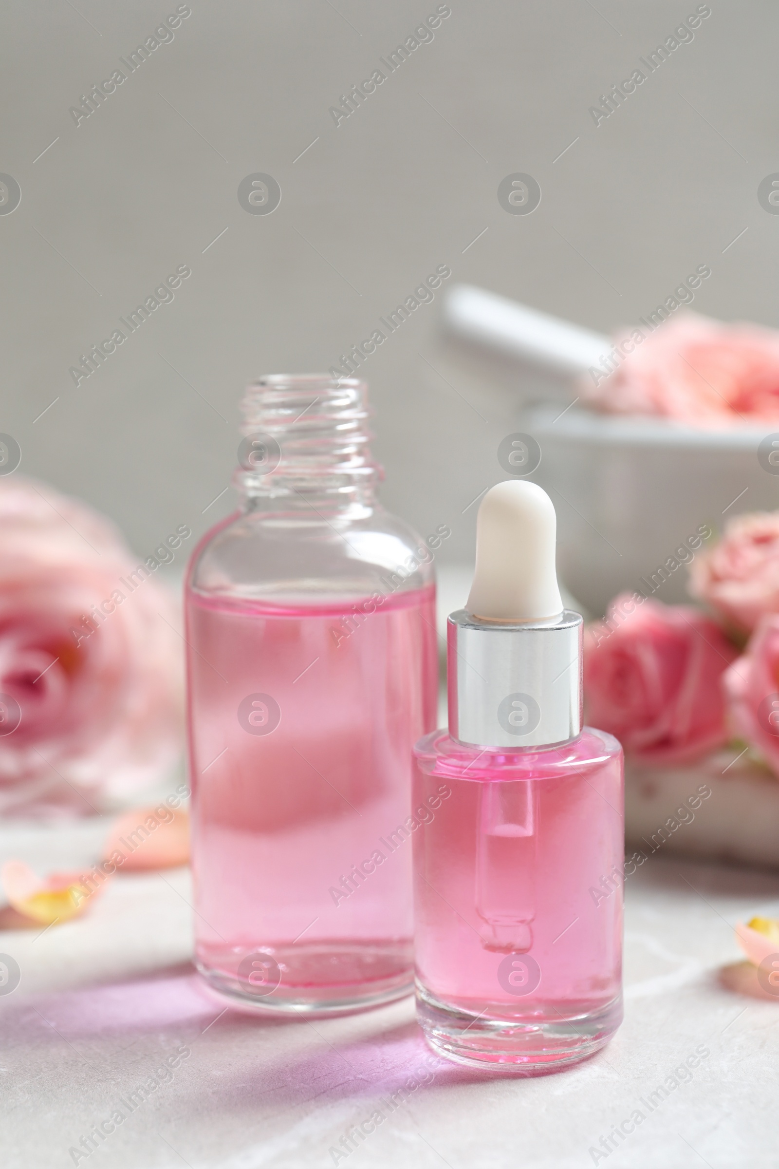 Photo of Bottles of rose essential oil and fresh flowers on table, space for text