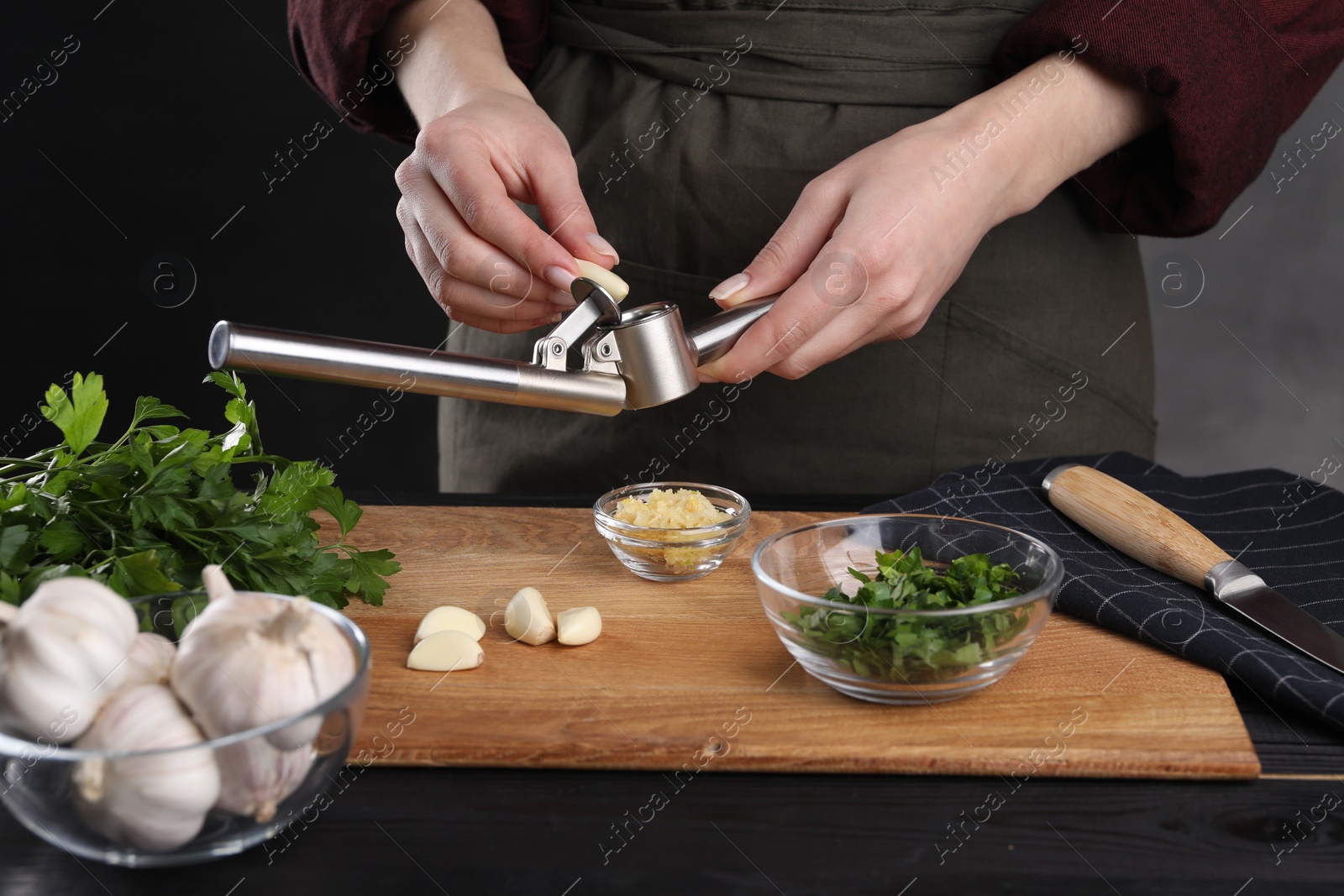 Photo of Woman squeezing garlic with press at black wooden table, closeup