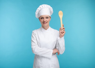 Photo of Happy woman chef in uniform holding wooden spoon on light blue background