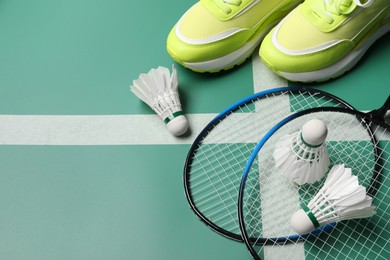 Feather badminton shuttlecocks, rackets and sneakers on court, above view. Space for text