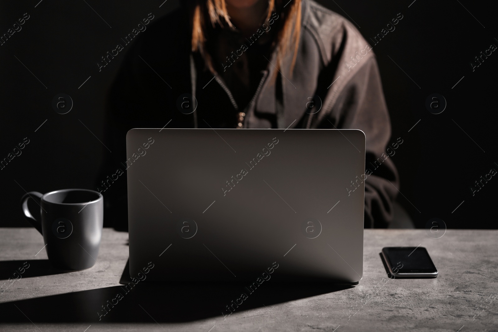 Photo of Woman with laptop and smartphone at table in darkness, closeup