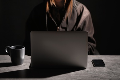 Photo of Woman with laptop and smartphone at table in darkness, closeup