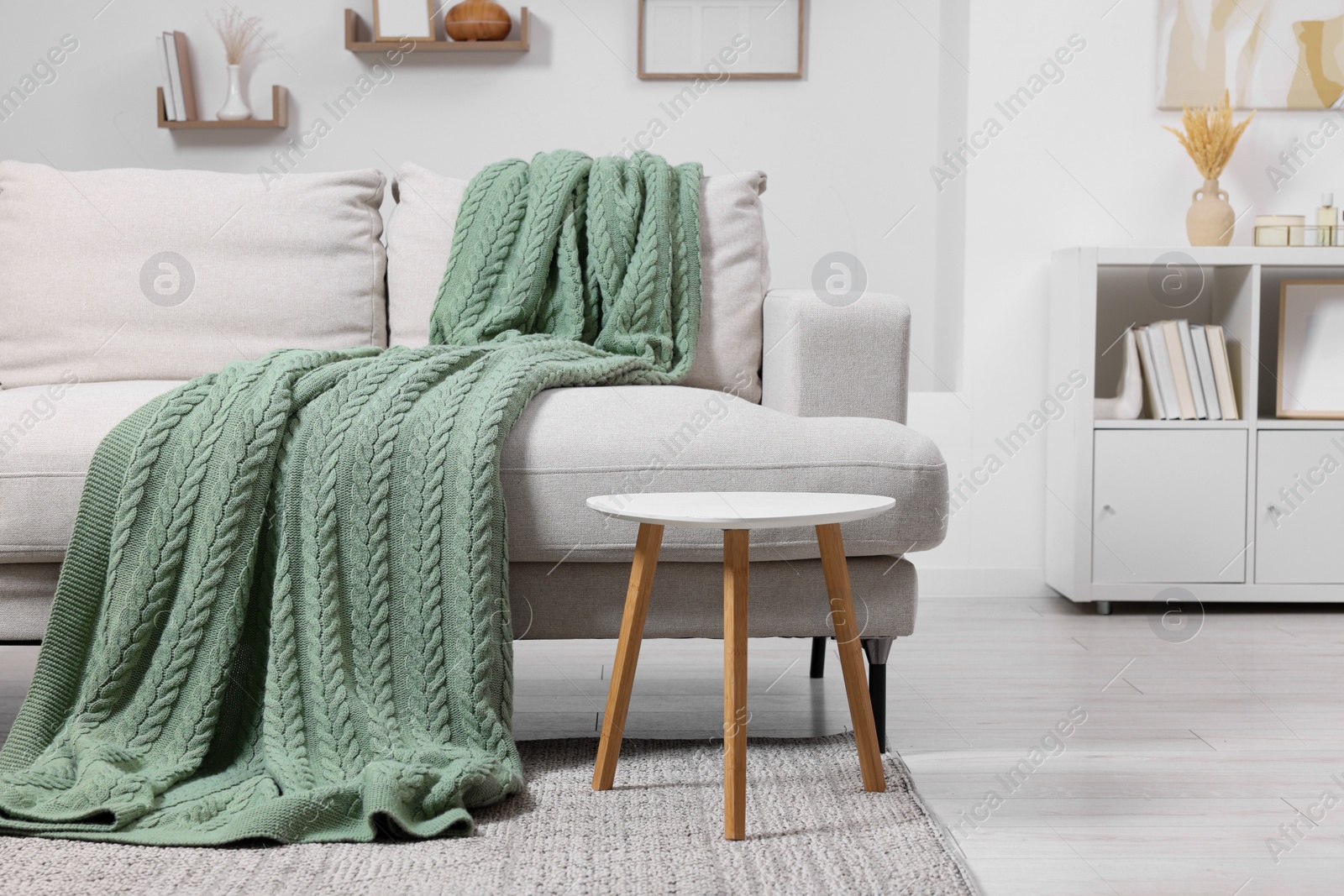 Photo of Knitted plaid on comfortable sofa in living room. Space for text