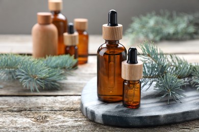 Photo of Bottles of spruce essential oil and fresh twigs on wooden table, space for text