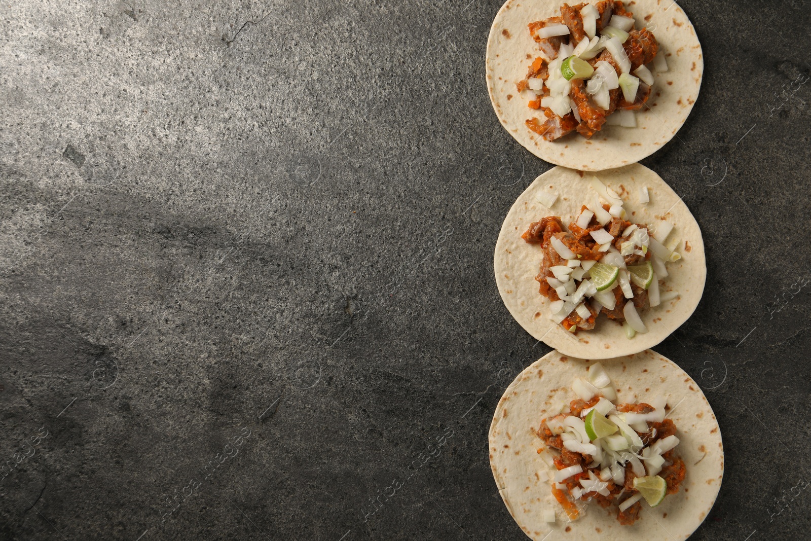 Photo of Delicious tacos with vegetables, meat and lime on grey textured table, flat lay. Space for text