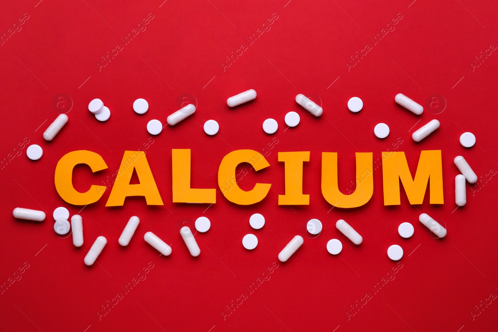 Photo of Word Calcium made of orange letters and white pills on red background, flat lay