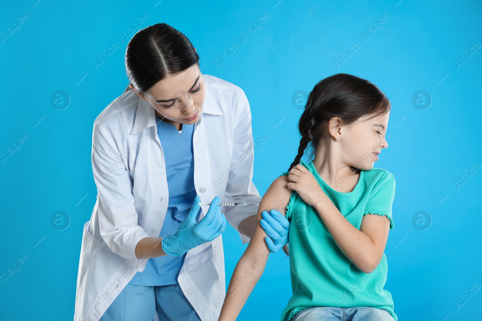 Photo of Doctor vaccinating little child on light blue background
