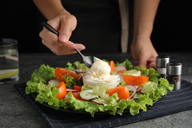 Photo of Woman dressing delicious vegetable salad with mayonnaise at grey table, closeup