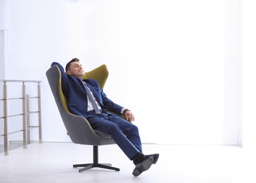 Photo of Young businessman sitting in comfortable armchair indoors. Space for text