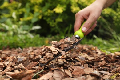 Photo of Woman mulching soil with bark chips in garden, closeup