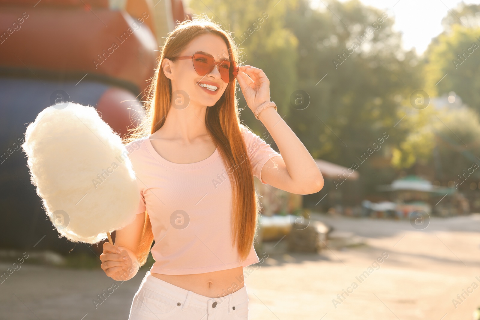 Photo of Smiling woman with cotton candy outdoors on sunny day. Space for text