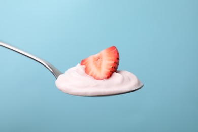 Photo of Delicious natural yogurt with fresh strawberry in spoon on light blue background