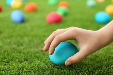 Little child taking Easter egg from green grass, closeup