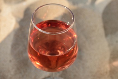 Photo of Glass of tasty rose wine on sand, closeup