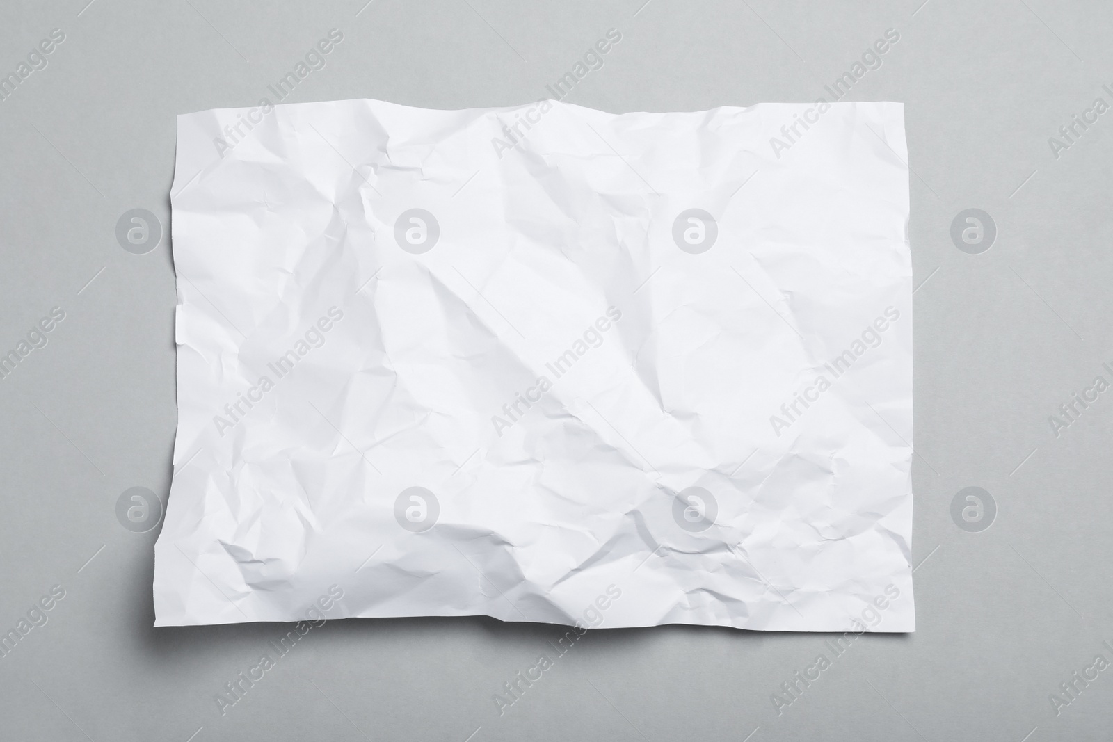 Photo of Sheet of white crumpled paper on grey background, top view