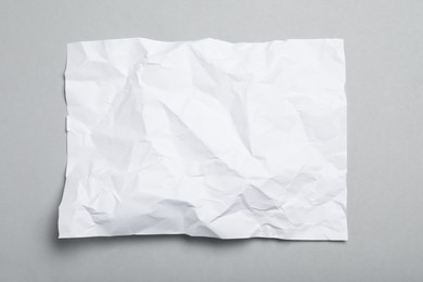 Sheet of white crumpled paper on grey background, top view