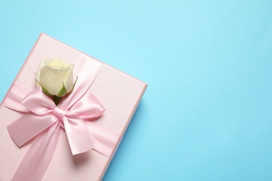 Photo of Pink gift box with flower on light blue background, top view. Space for text
