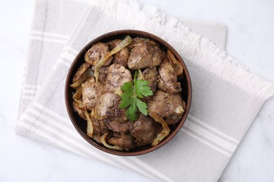 Photo of Tasty fried chicken liver with onion and parsley in bowl on white table, top view