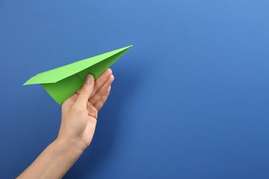 Photo of Woman holding paper plane on blue background, closeup. Space for text