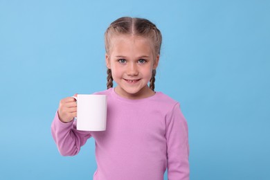 Happy girl with white ceramic mug on light blue background