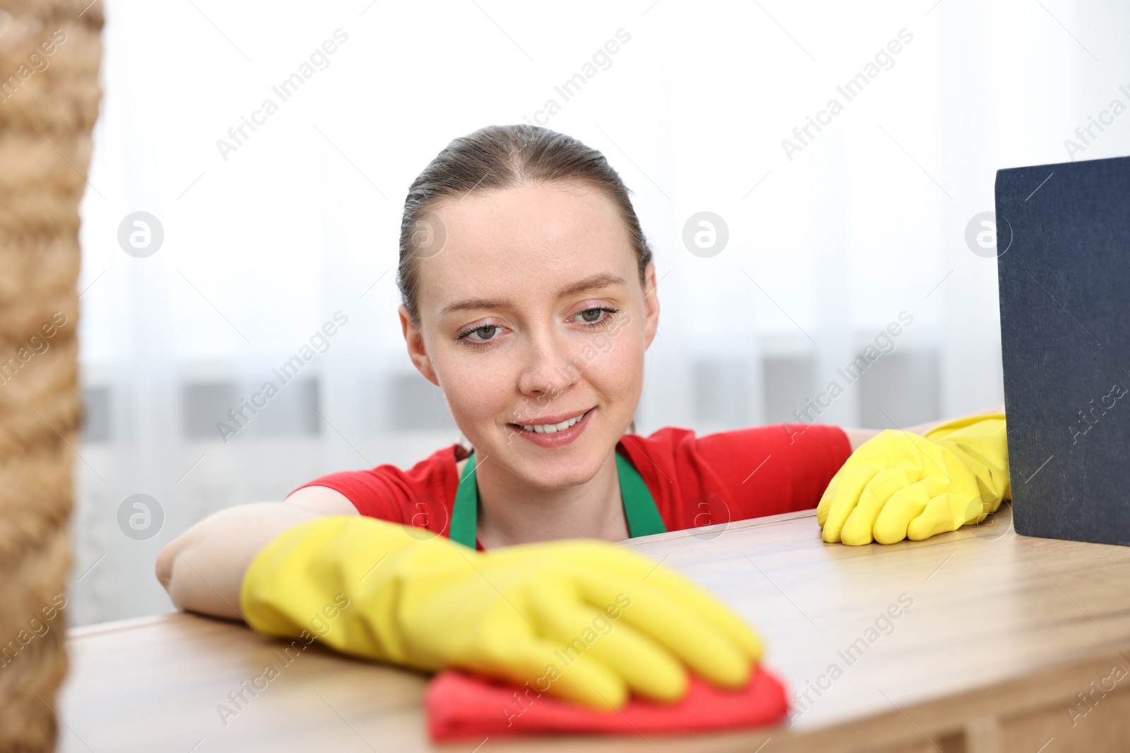 Photo of Woman cleaning wooden table with rag at home