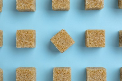 Photo of Brown sugar cubes on light blue background, flat lay