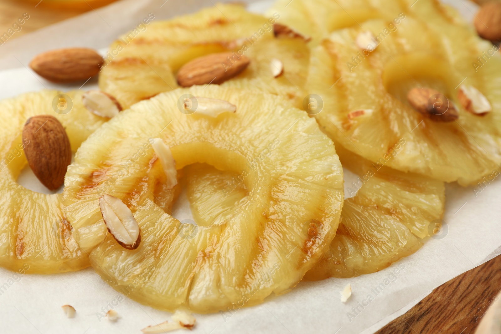 Photo of Tasty grilled pineapple slices and almonds on parchment paper, closeup