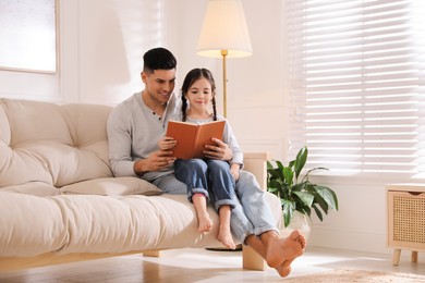 Photo of Father and daughter reading book on sofa at home