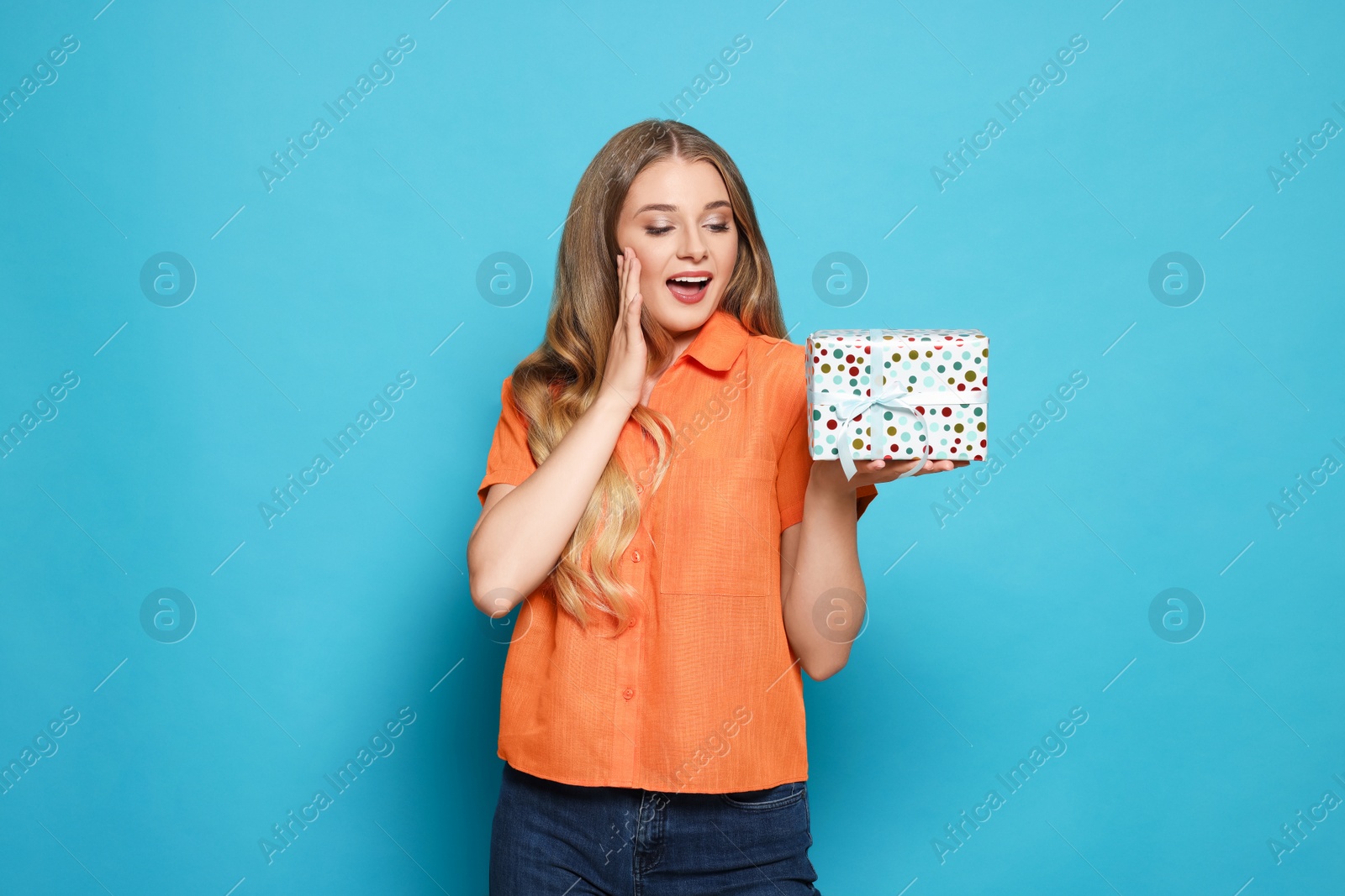 Photo of Emotional young woman holding colorful gift box on light blue background