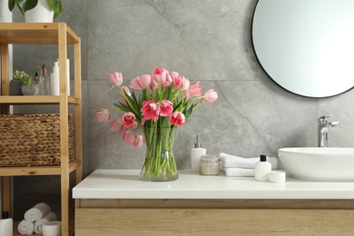 Vase with beautiful pink tulips and toiletries near sink in bathroom