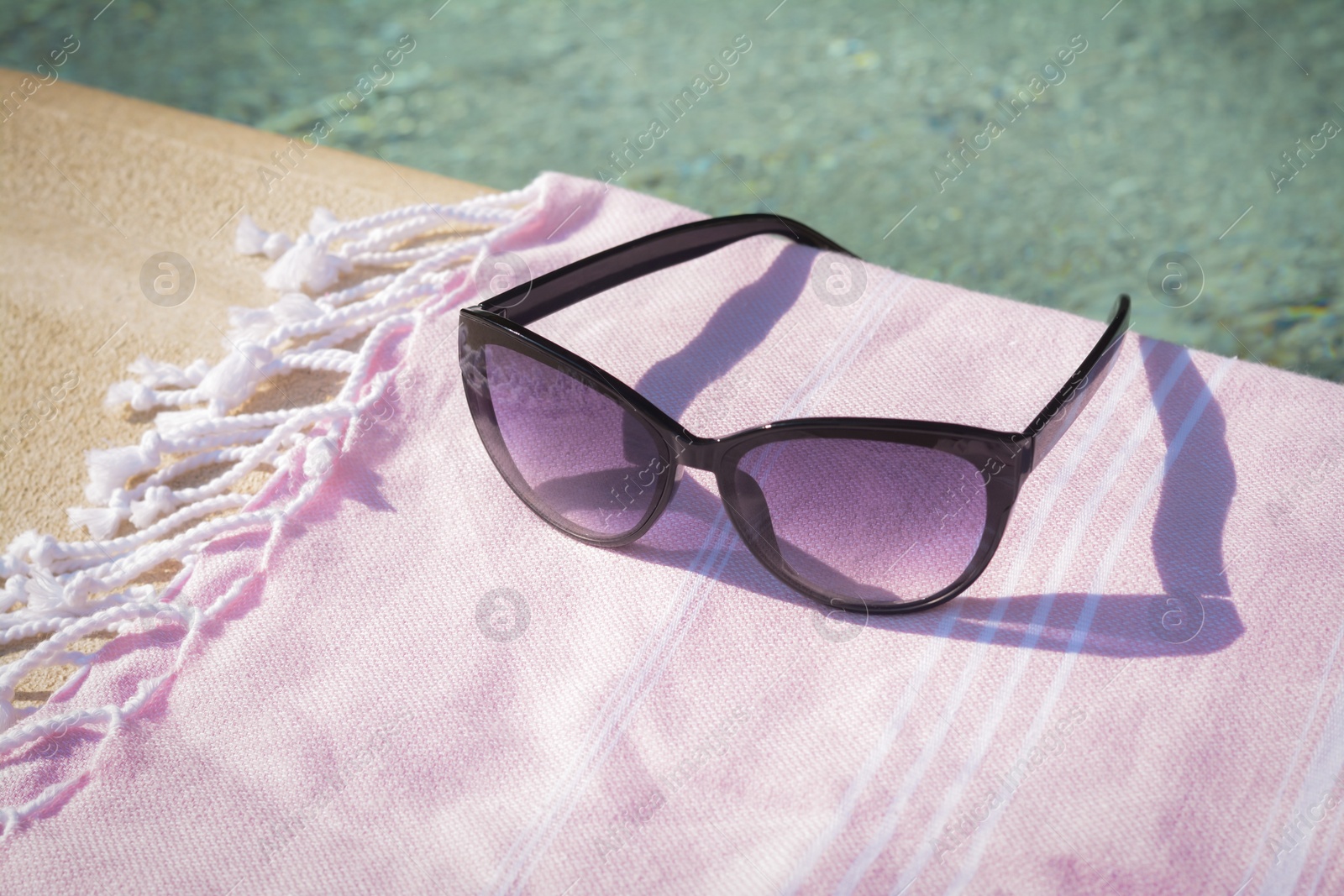 Photo of Stylish sunglasses and blanket near outdoor pool on sunny day