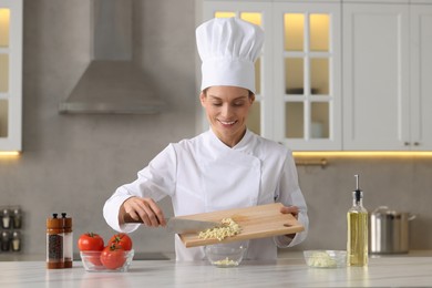 Professional chef putting cut garlic into bowl at white marble table indoors