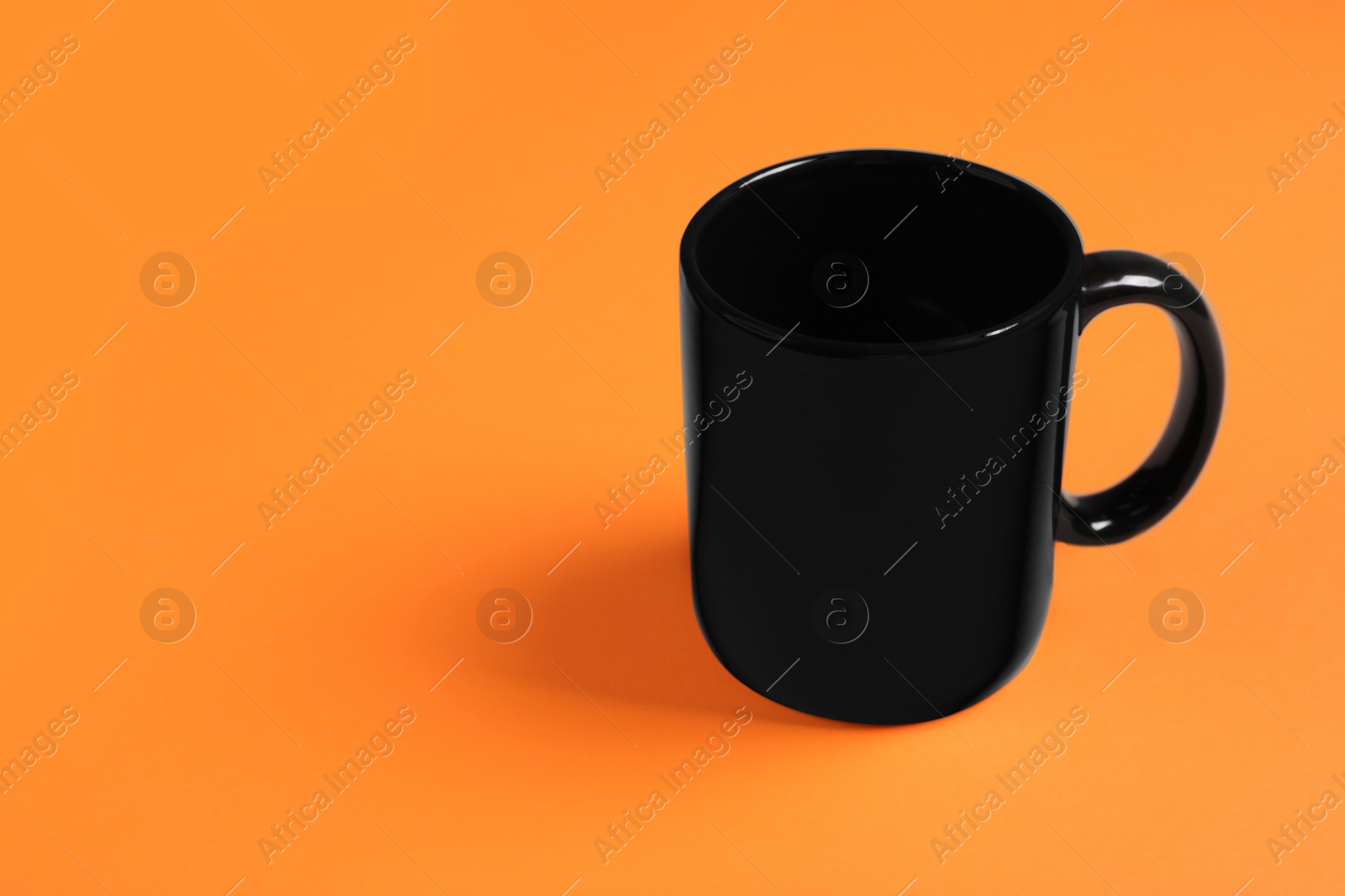 One black ceramic mug on orange background, space for text Photo of One black ceramic mug on orange background, space for text