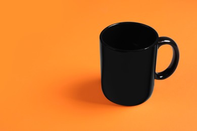 Photo of One black ceramic mug on orange background, space for text