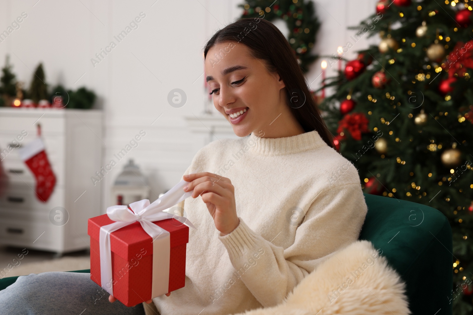 Photo of Happy young woman opening Christmas gift at home