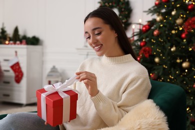Happy young woman opening Christmas gift at home