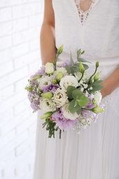 Bride holding beautiful bouquet with Eustoma flowers indoors, closeup