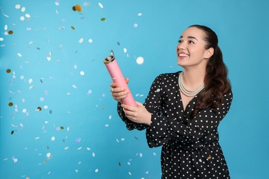 Photo of Young woman blowing up party popper on light blue background