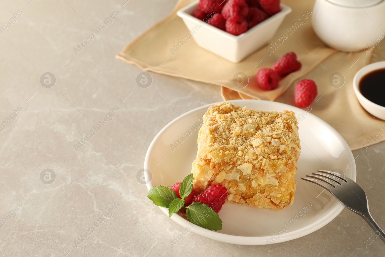 Photo of Piece of delicious Napoleon cake, raspberries and fork on beige table, space for text
