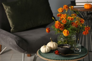 Photo of Beautiful autumn flowers, cup of coffee and pumpkins on side table indoors, space for text