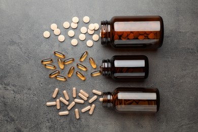 Overturned bottles with different dietary supplements on grey table, flat lay